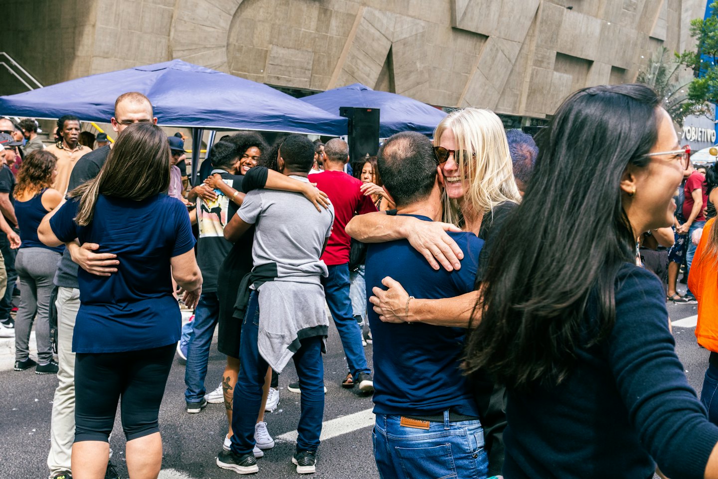 A diverse group of people hugging outdoors near blue tents.